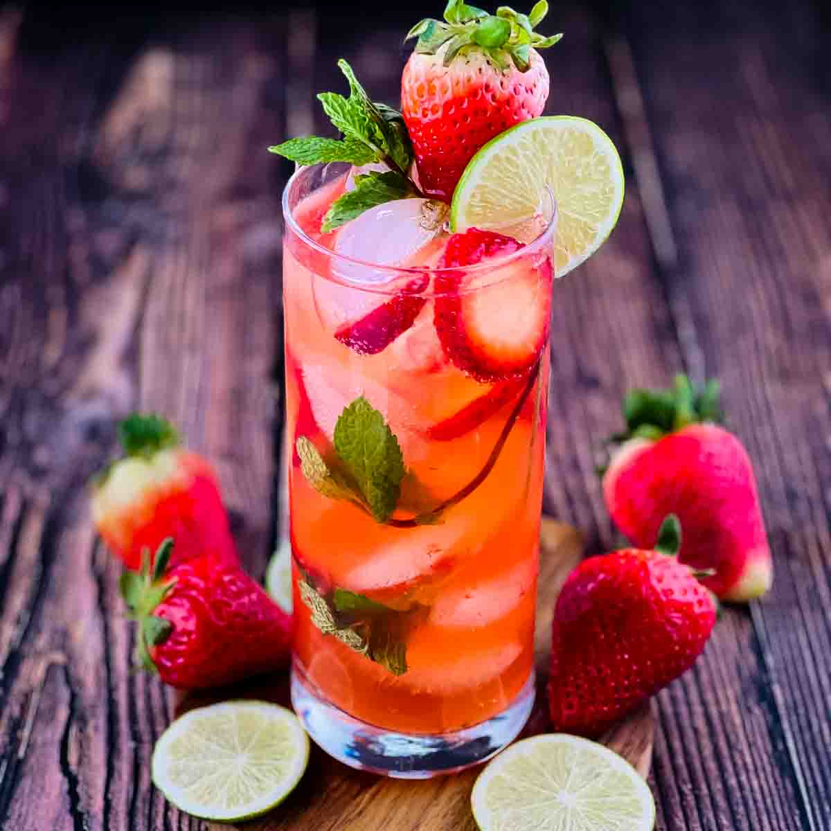 A highball glass of a strawberry mojito garnished with fresh strawberries and lime wheels.