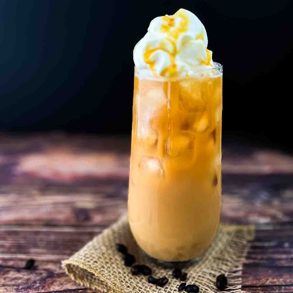A tall glass of caramel iced coffee topped with whipped cream and caramel syrup.