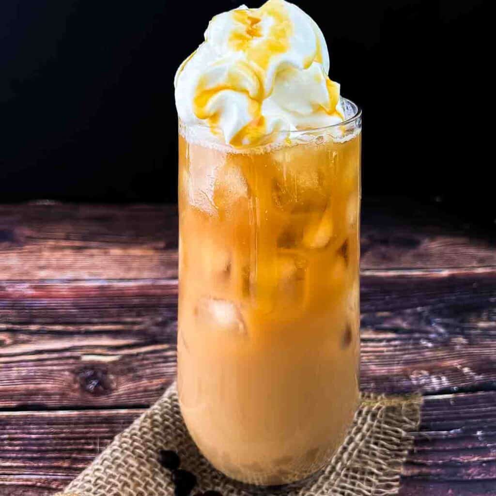A tall glass of McDonalds caramel iced coffee, topped with whipped cream and caramel syrup.