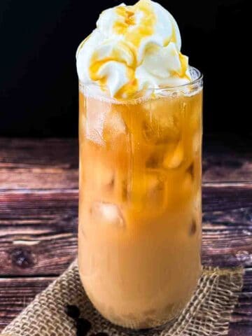 A tall glass of McDonalds caramel iced coffee, topped with whipped cream and caramel syrup.