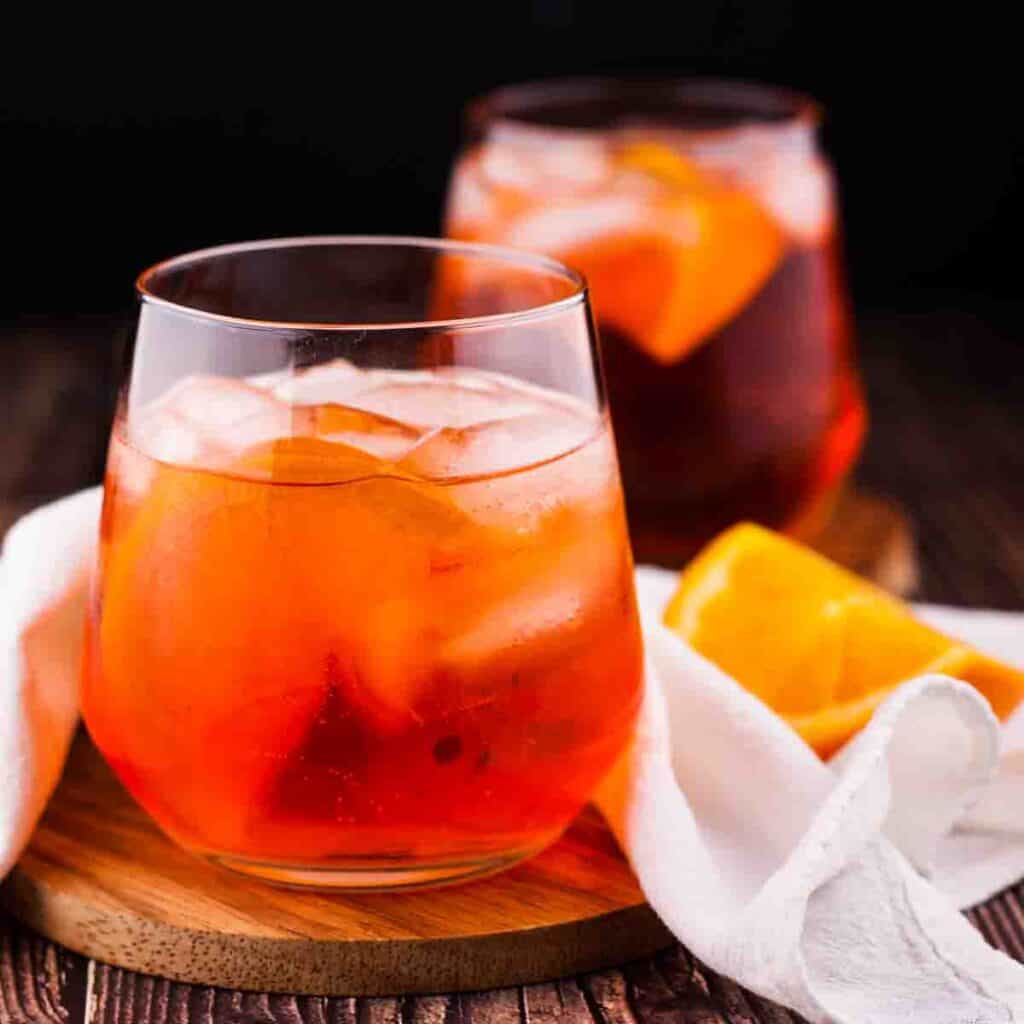 Two glasses of Aperol Spritz in stemless wine glasses, garnished with an orange wedge.