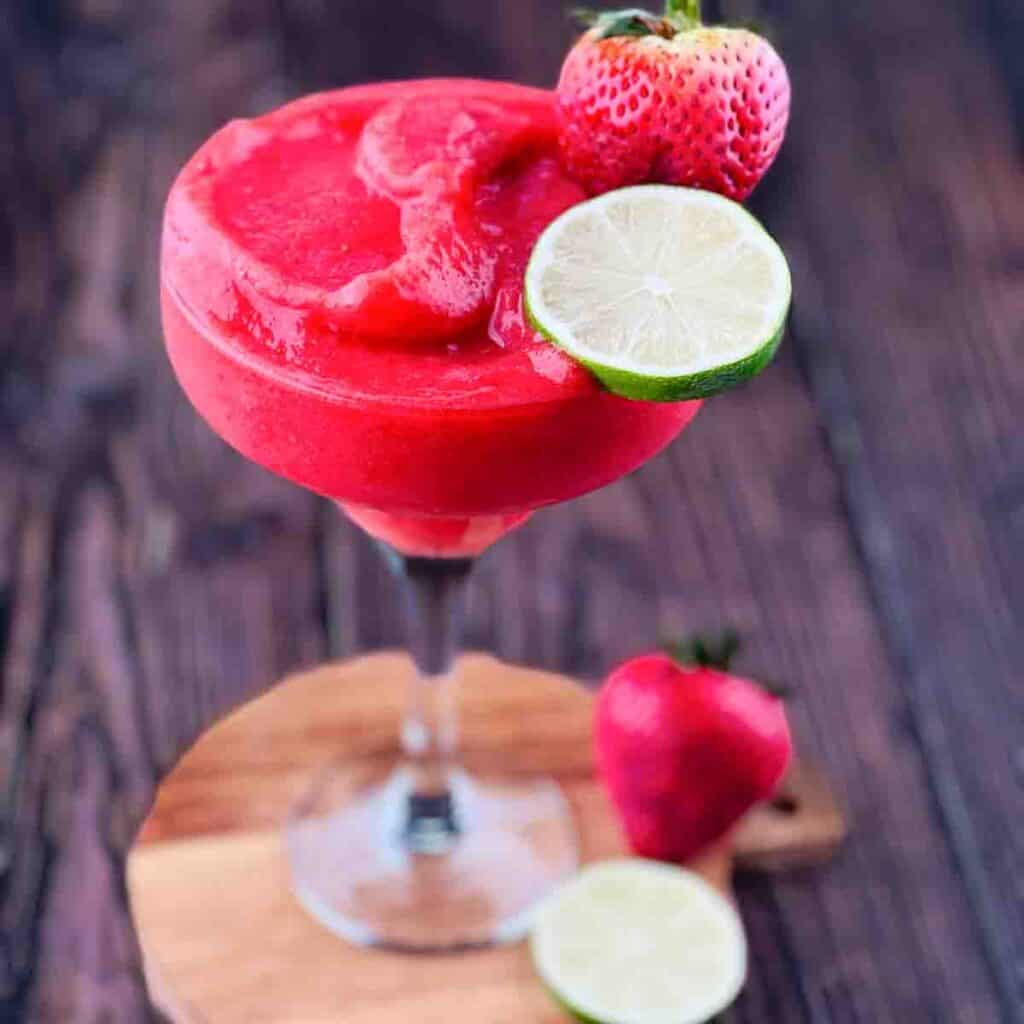 A frozen strawberry daiquiri in a margarita glass, garnished with a lime wheel and strawberries.