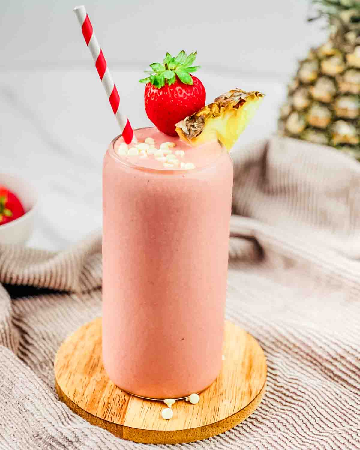 A tall glass of Tropical Smoothie Bahama Mama copycat recipe, garnished with a strawberry, pineapple, and white chocolate chips.