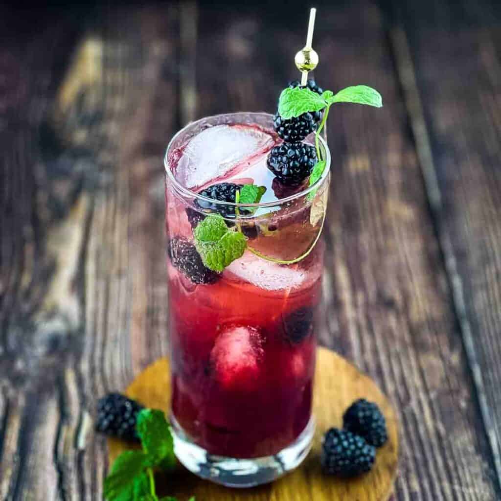 A highball glass filled with a blackberry mojito.