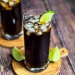 Two highball glasses with a Cuba Libre cocktail garnished with a lime wedge.