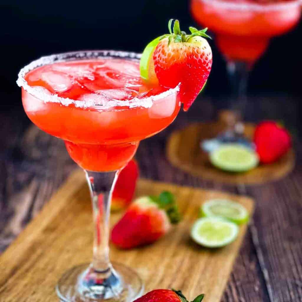 Strawberry margarita on the rocks in a margarita glass with a salted rim.