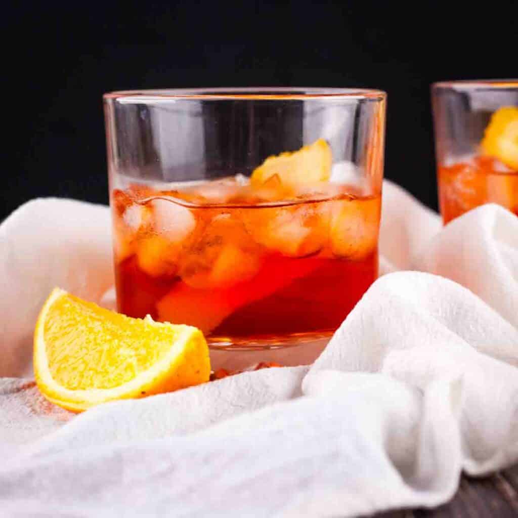A rocks glass filled with an aperol negroni garnished with an orange twist.