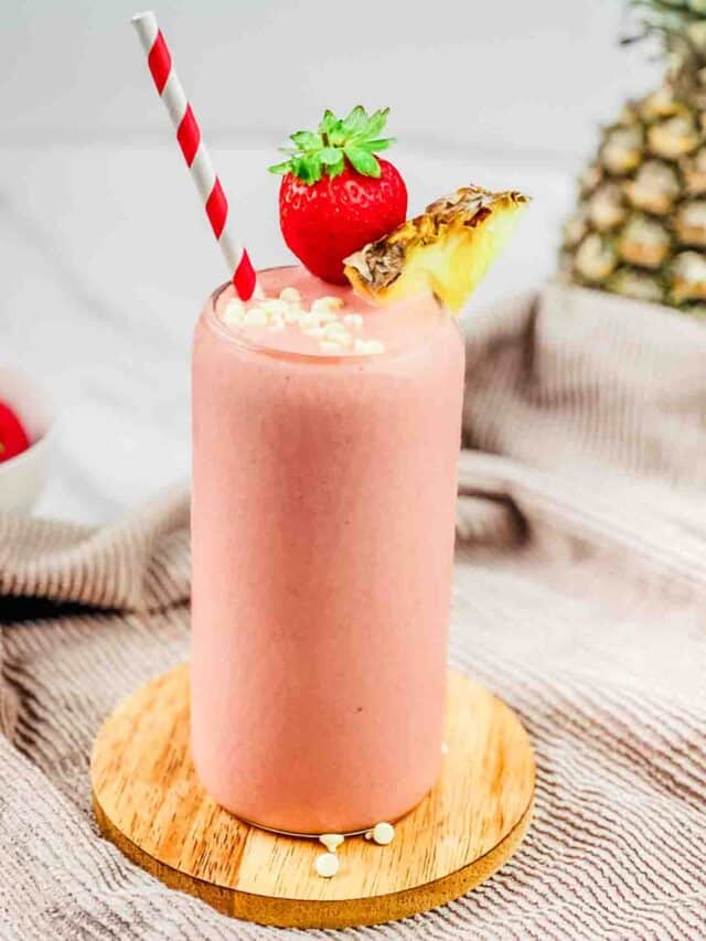A tall glass of Tropical Smoothie Bahama Mama copycat recipe, garnished with a strawberry, pineapple, and white chocolate chips.