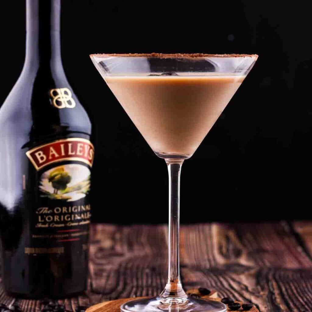 Espresso martini in a glass with a bottle of Baileys Irish cream in the background.