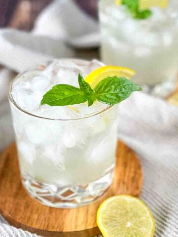 Two small cocktail glasses of gin basil smash garnished with fresh basil and lemon.