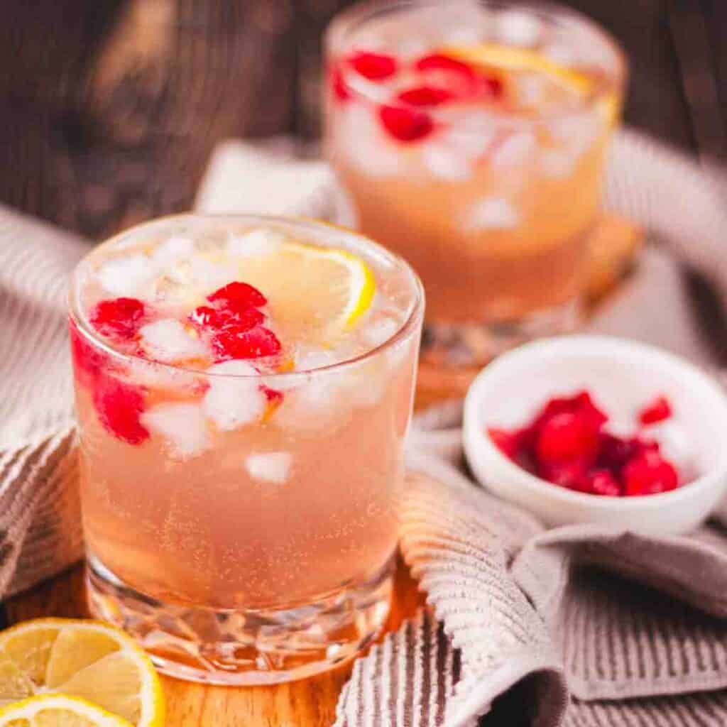 Raspberry gin spritz in two rocks glasses, garnished with fresh raspberries and a slice of lemon.