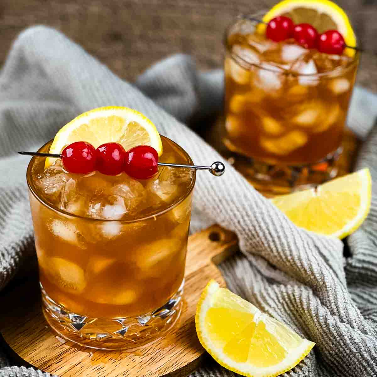 Two old-fashioned glasses with the rum sour cocktail, garnished with cherries and lemons.