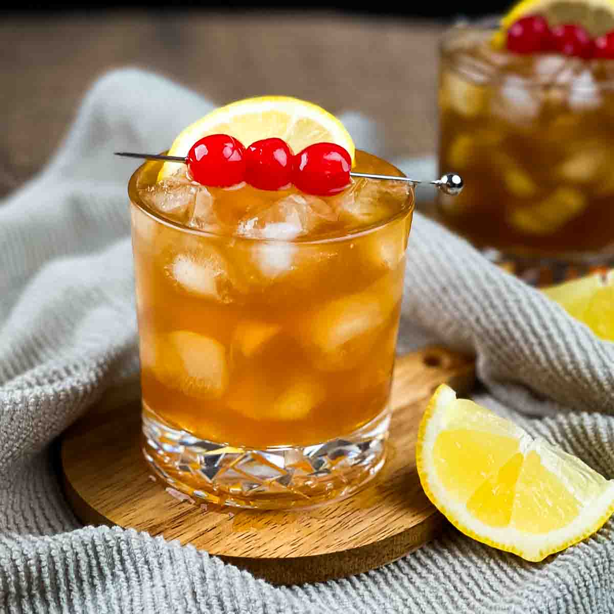 Two glasses of rum sour garnished with a lemon wedge and three maraschino cherries on a serving pick.