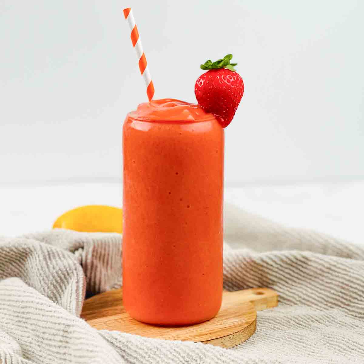 The Sunrise Sunset smoothie in a tall glass with an orange and white striped straw.