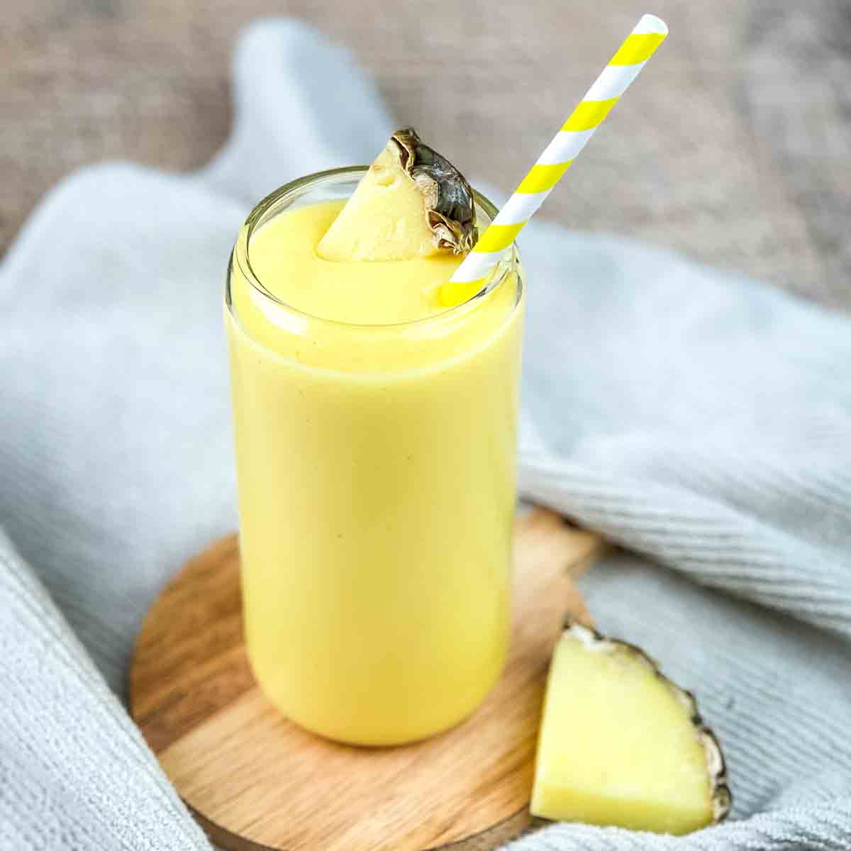 A tall glass of a mango pineapple smoothie with a yellow and white striped straw.