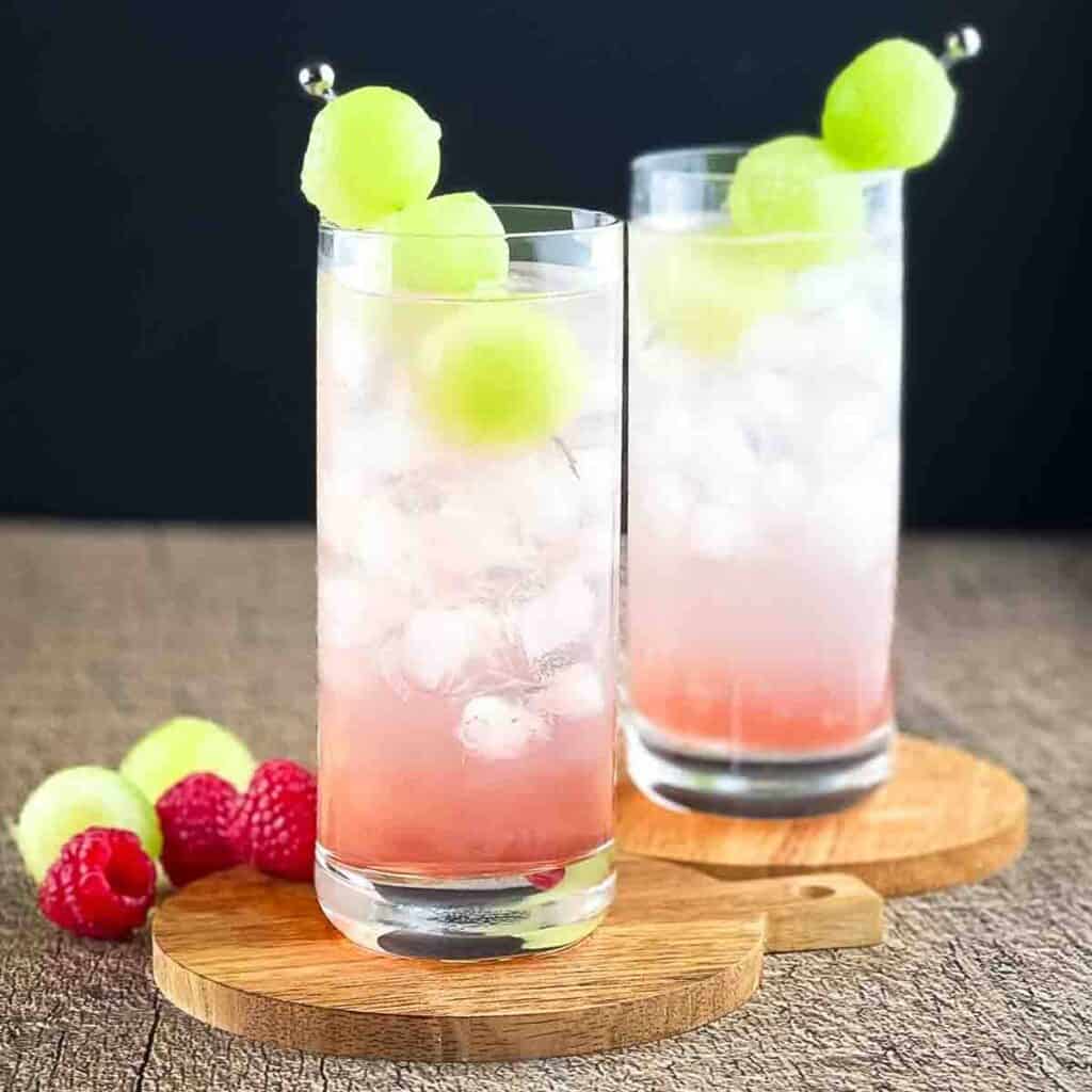 Two tall glasses of chambord vodka lemonade, garnished with three melon balls.