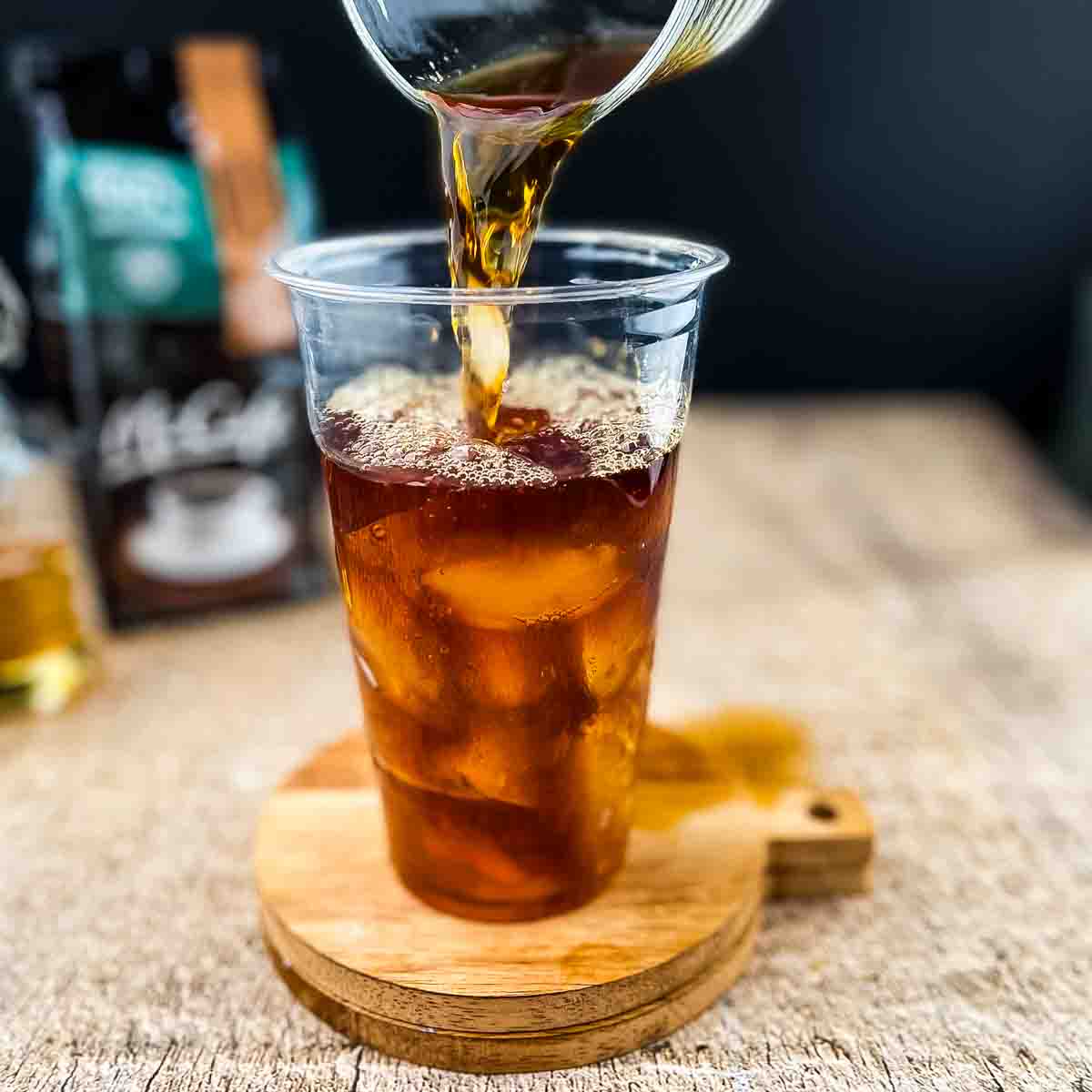 Cold coffee being poured over ice cubes in a tall glass.
