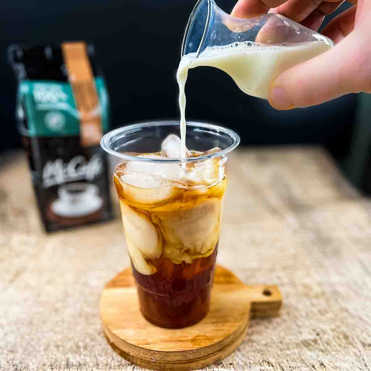 Milk being poured into the glass with the coffee, syrup, and ice cubes.