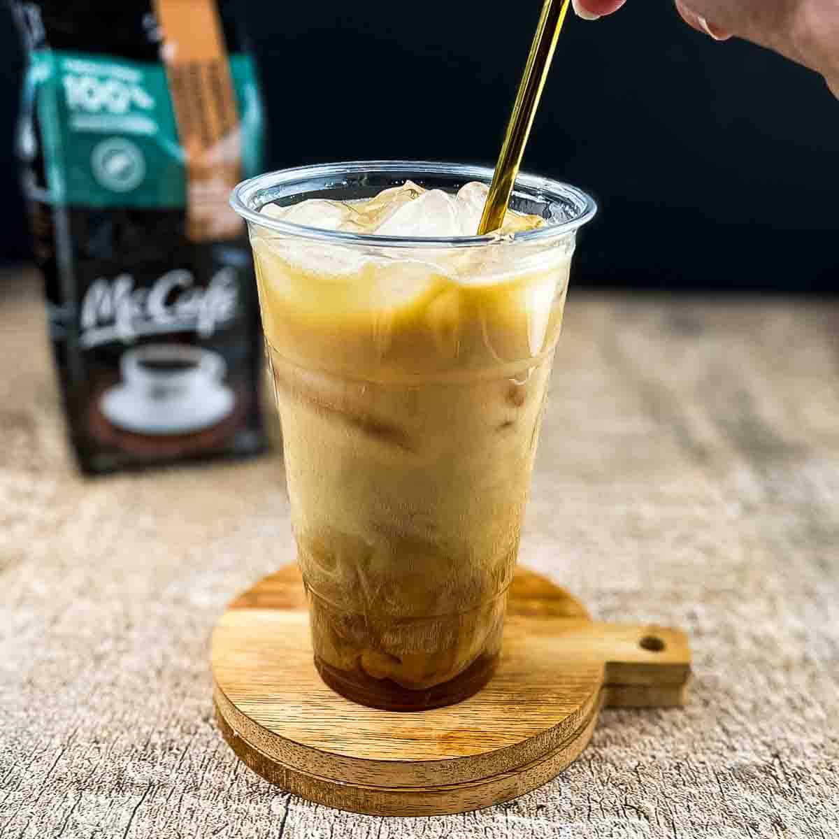 A hand using a gold straw to mix the ingredients for the McDonalds iced coffee together.
