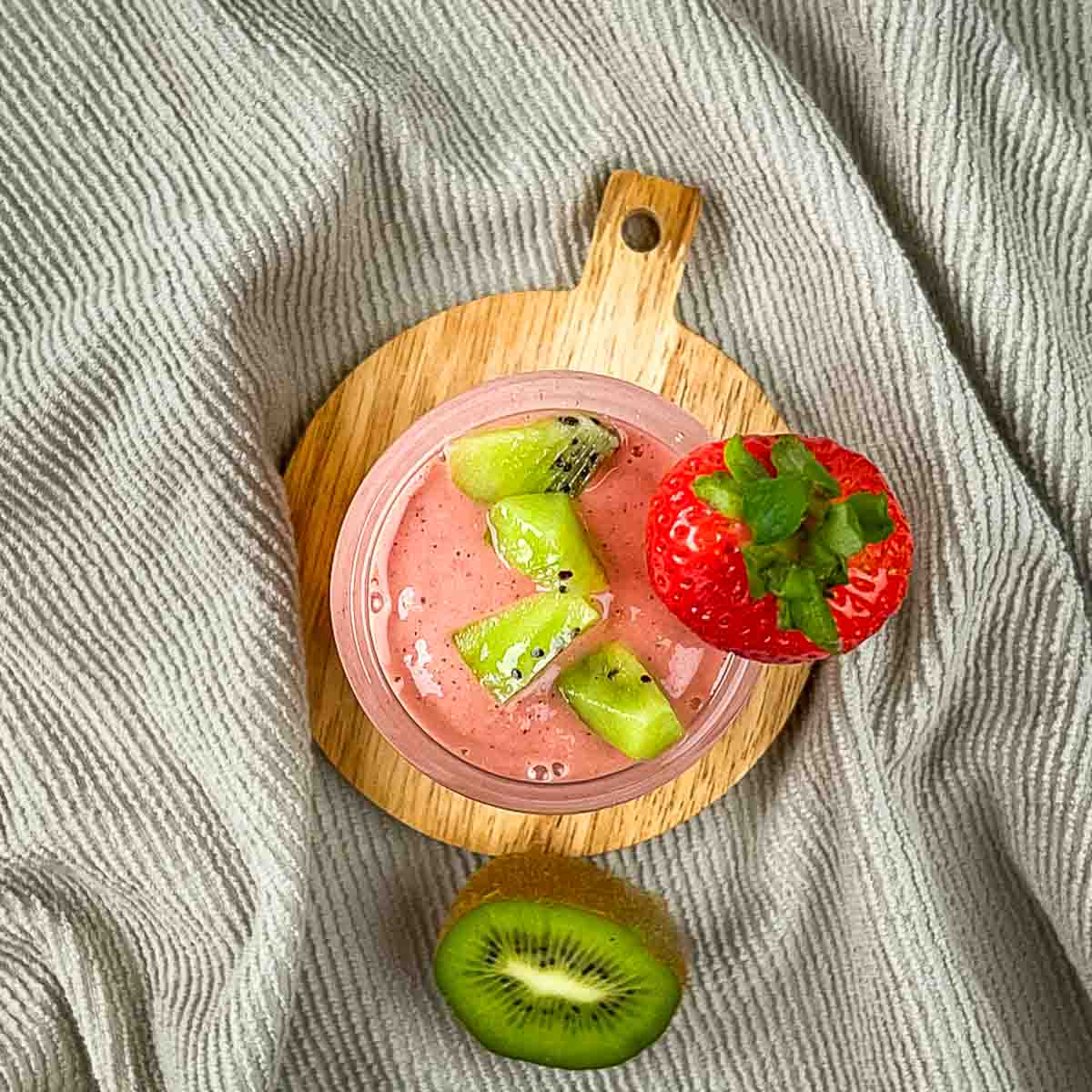 The smoothie in a tall glass garnished with chopped kiwi and a fresh strawberry.