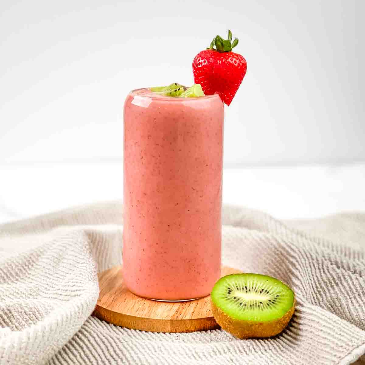 A tall glass filled with kiwi tropical smoothie, garnished with a fresh kiwi and strawberry.