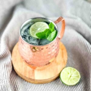 A copper mug filled with a Moscow Mule with rum, garnished with fresh mint leaves and a lime wheel.