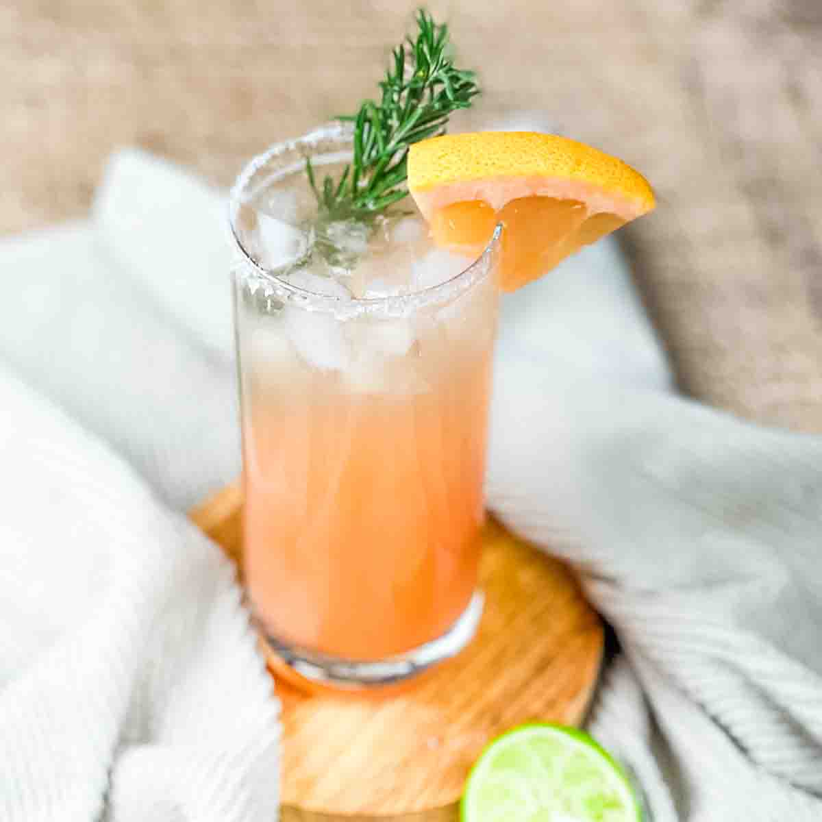 Non alcoholic grapefruit paloma in a tall glass, garnished with a grapefruit wedge and fresh rosemary.