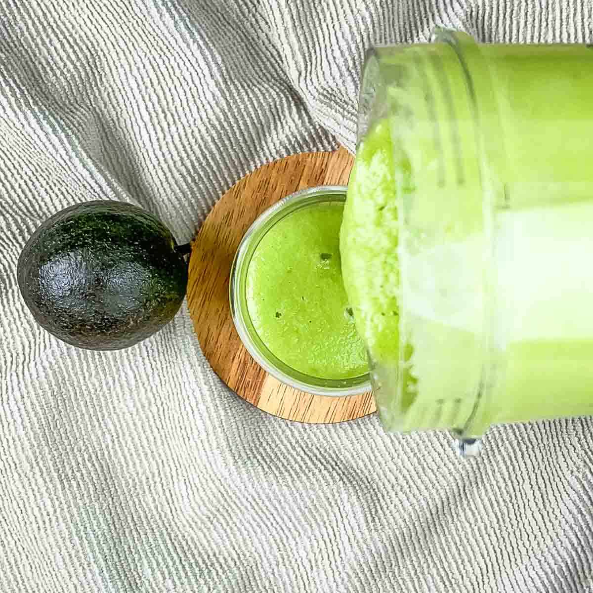 The thick green smoothie  being poured into a tall glass.
