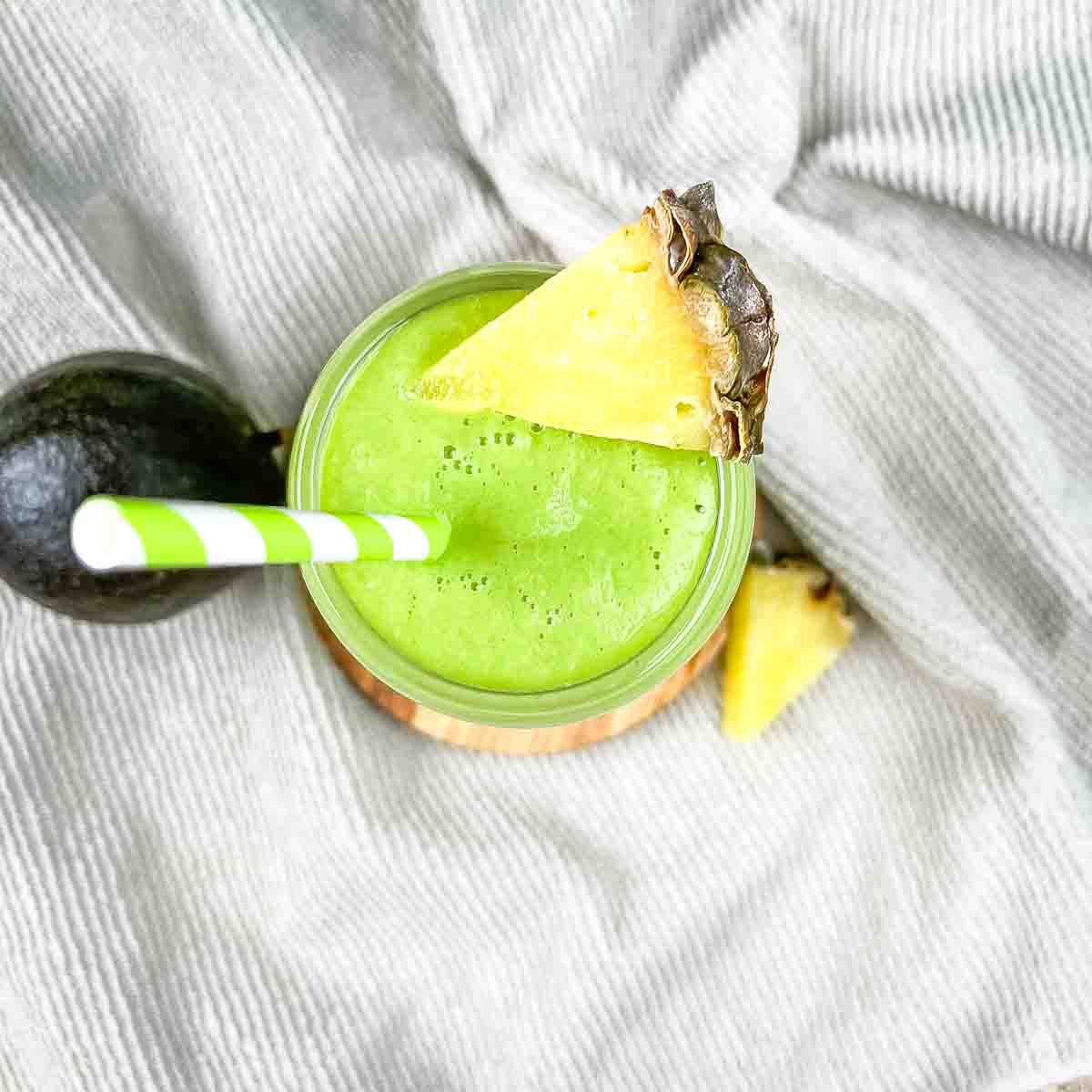 The green smoothie in a glass with a wedge of pineapple on the rim.
