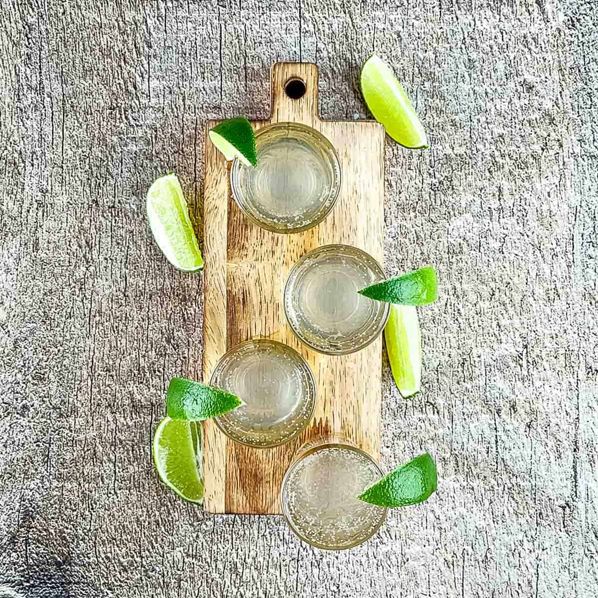 Four shot glasses garnished with lime wedges.