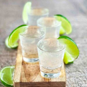 Four white tea shots on a wooden board, garnished with a lime wedge.