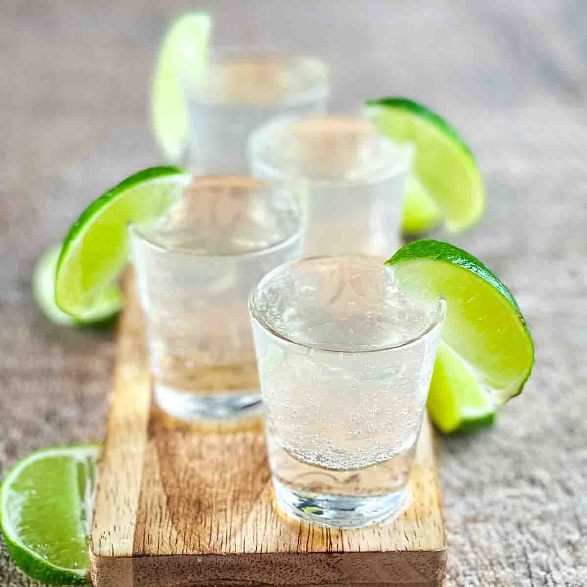 Four white tea shots on a wooden board, garnished with a lime wedge.