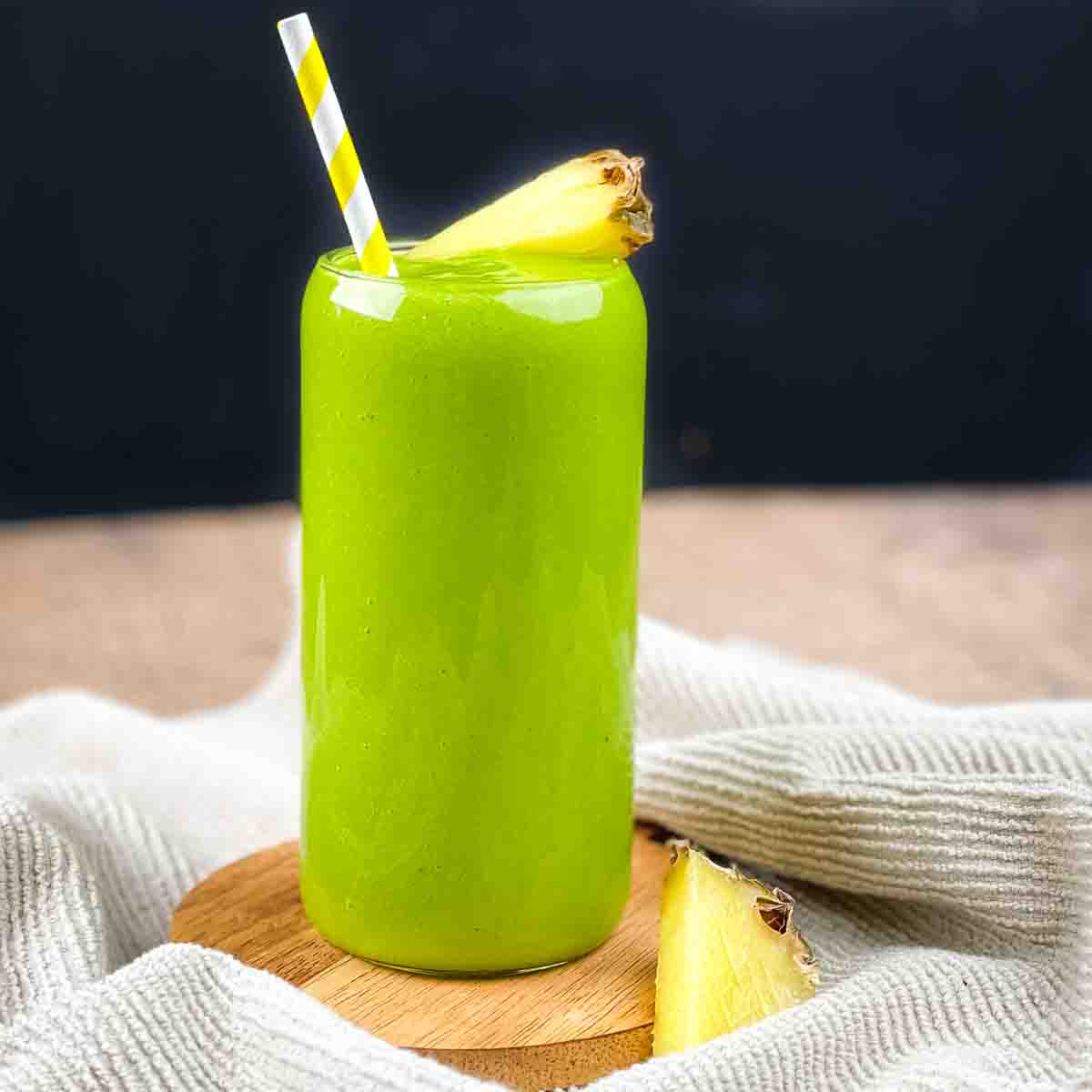 The green tropical smoothie in a tall glass with a white and yellow striped straw.