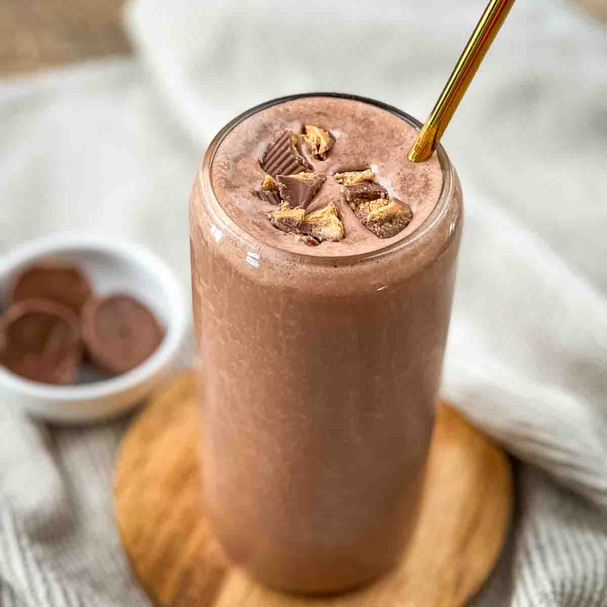 A tall glass filled with creamy peanut butter cup smoothie with a gold straw.