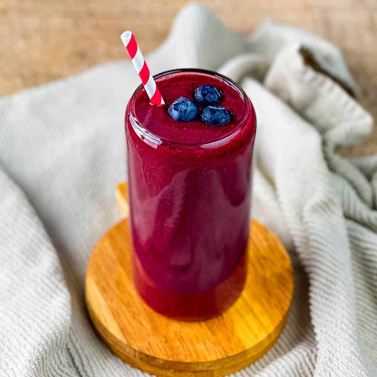 A tall glass of acai smoothie topped with fresh blueberries.