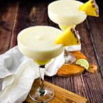 Two slushy frozen pineapple margaritas in a salt-rimmed glass, garnished with pineapple slices.