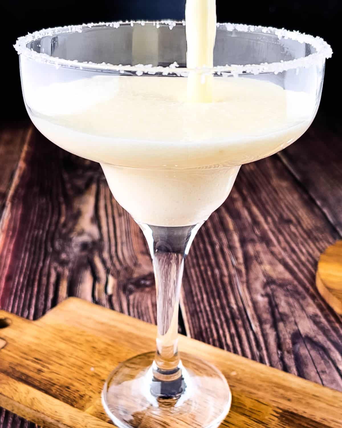 Blended pineapple margarita being poured into a salt-rimmed glass from the blender pitcher.