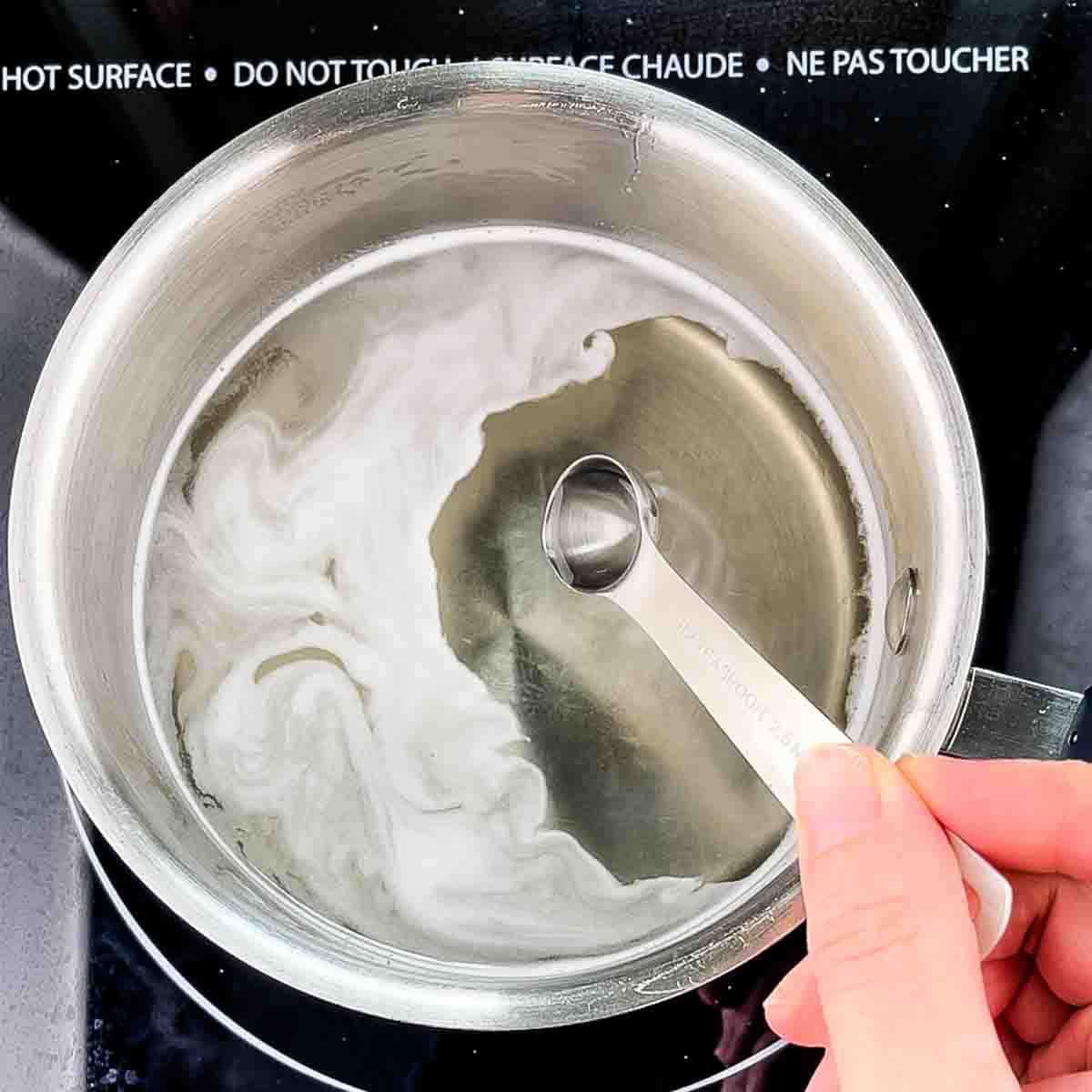Mint extract being added to the simple syrup in a saucepan.