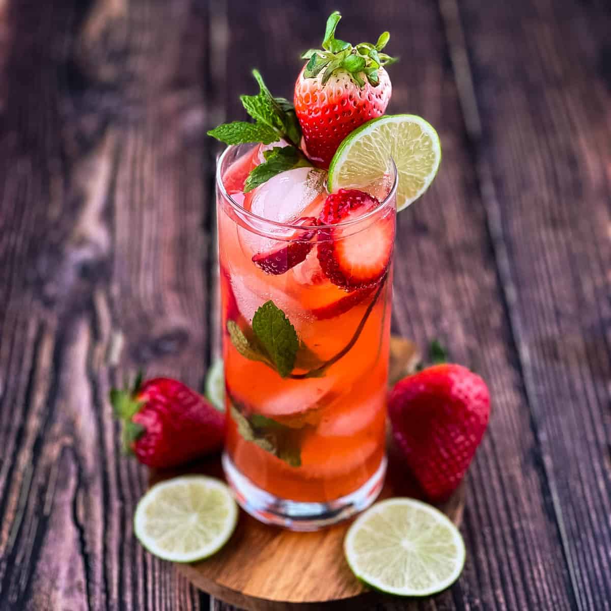 A tall glass filled with homemade strawberry mojito, garnished with fresh mint and berries and a lime wheel.