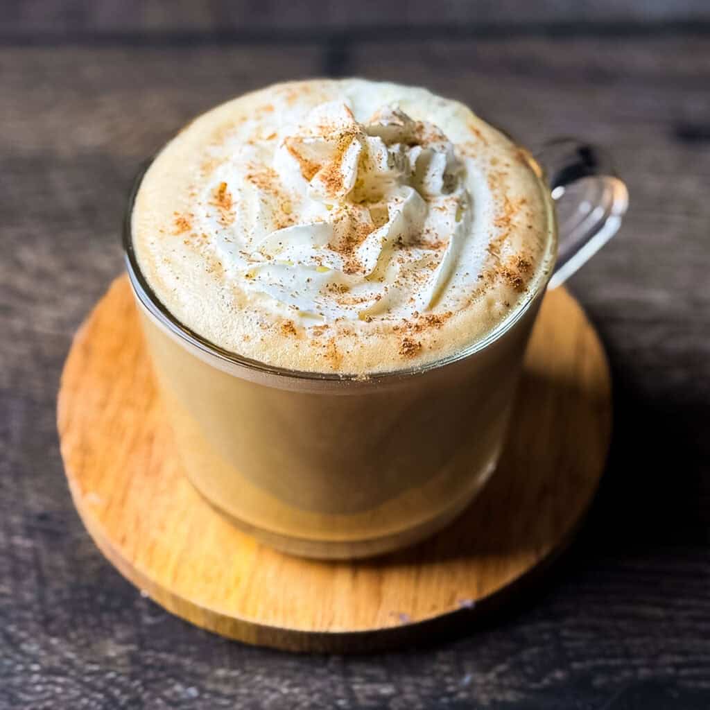 Eggnog chai latte topped with whipped cream and nutmeg in a glass mug, made with real eggnog and brewed chai tea.