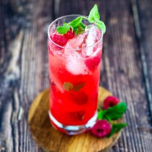 A tall glass of raspberry mint mojito with fresh mint and raspberries.
