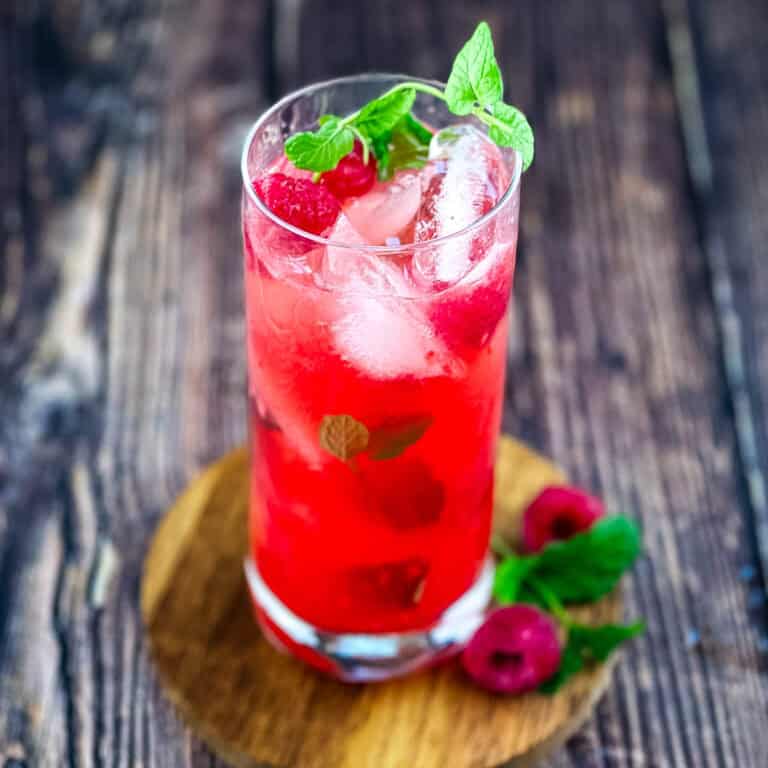 A tall glass of raspberry mint mojito with fresh mint and raspberries.