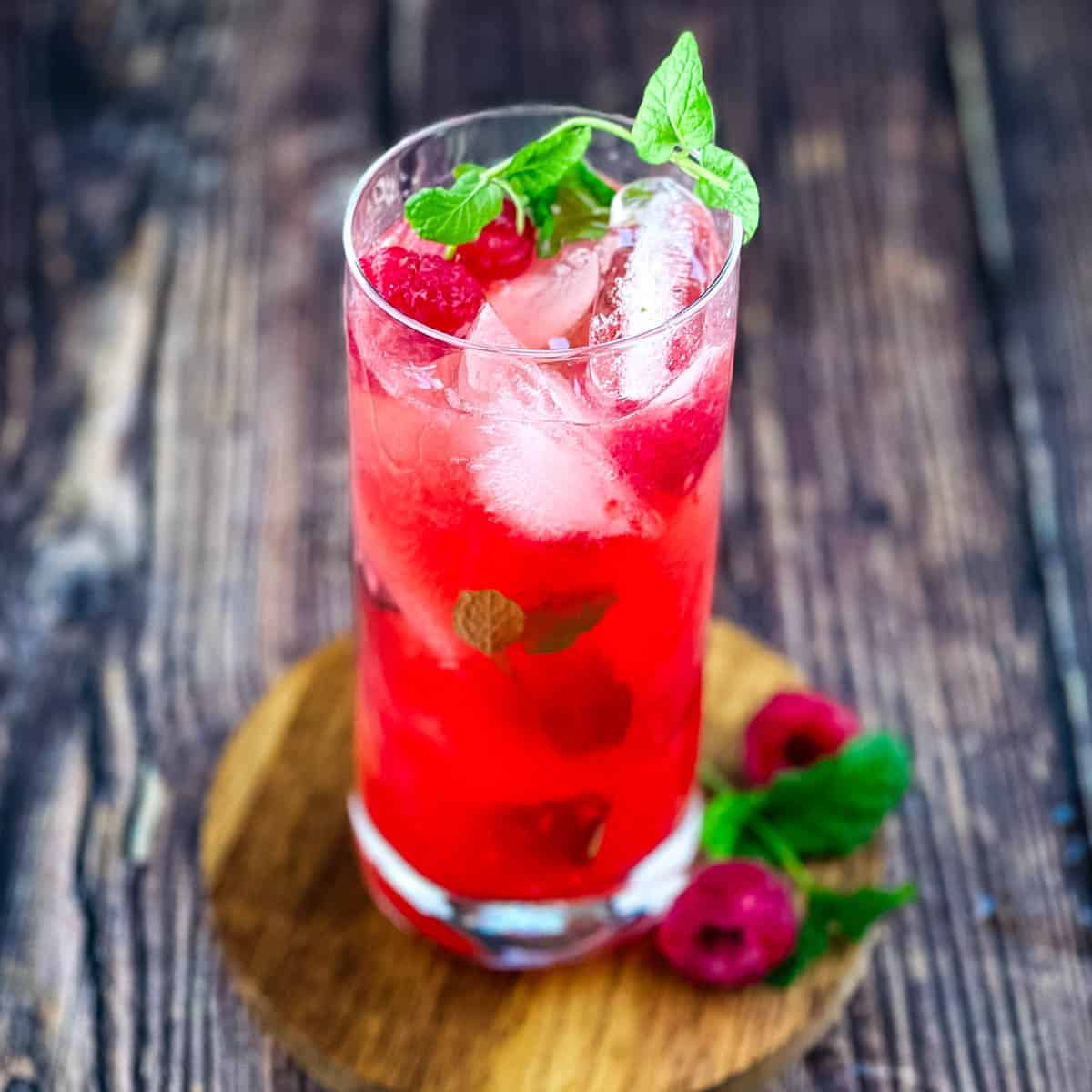 A tall glass of raspberry mint mojito with fresh mint and raspberries.