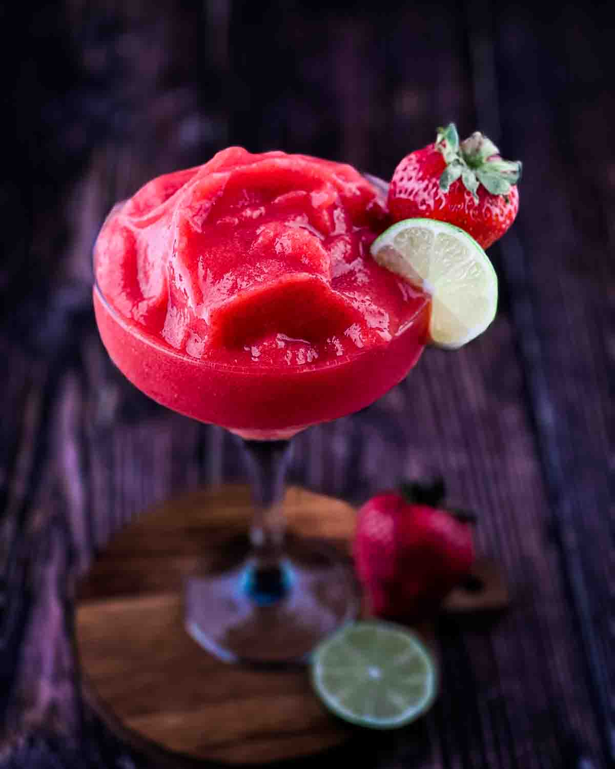 Frozen strawberry daiquiri in a tall glass garnished with a fresh strawberry and lime wheel.