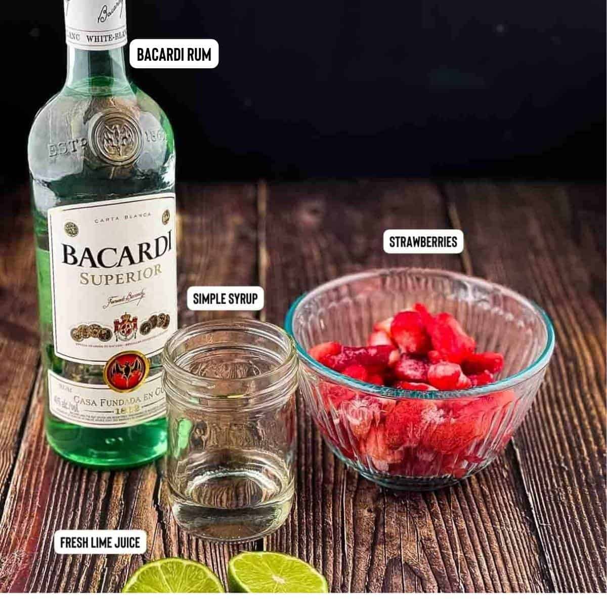 Labeled ingredients for a Bacardi strawberry daiquiri on a wooden table.